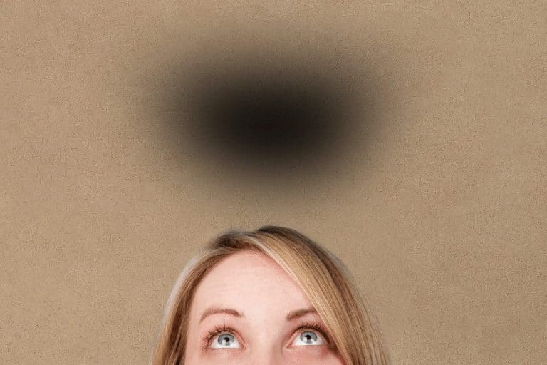 Eine Frau die besorgt nach oben schaut und eine schwarze Wolke sieht, die über ihrem Kopf hängt.